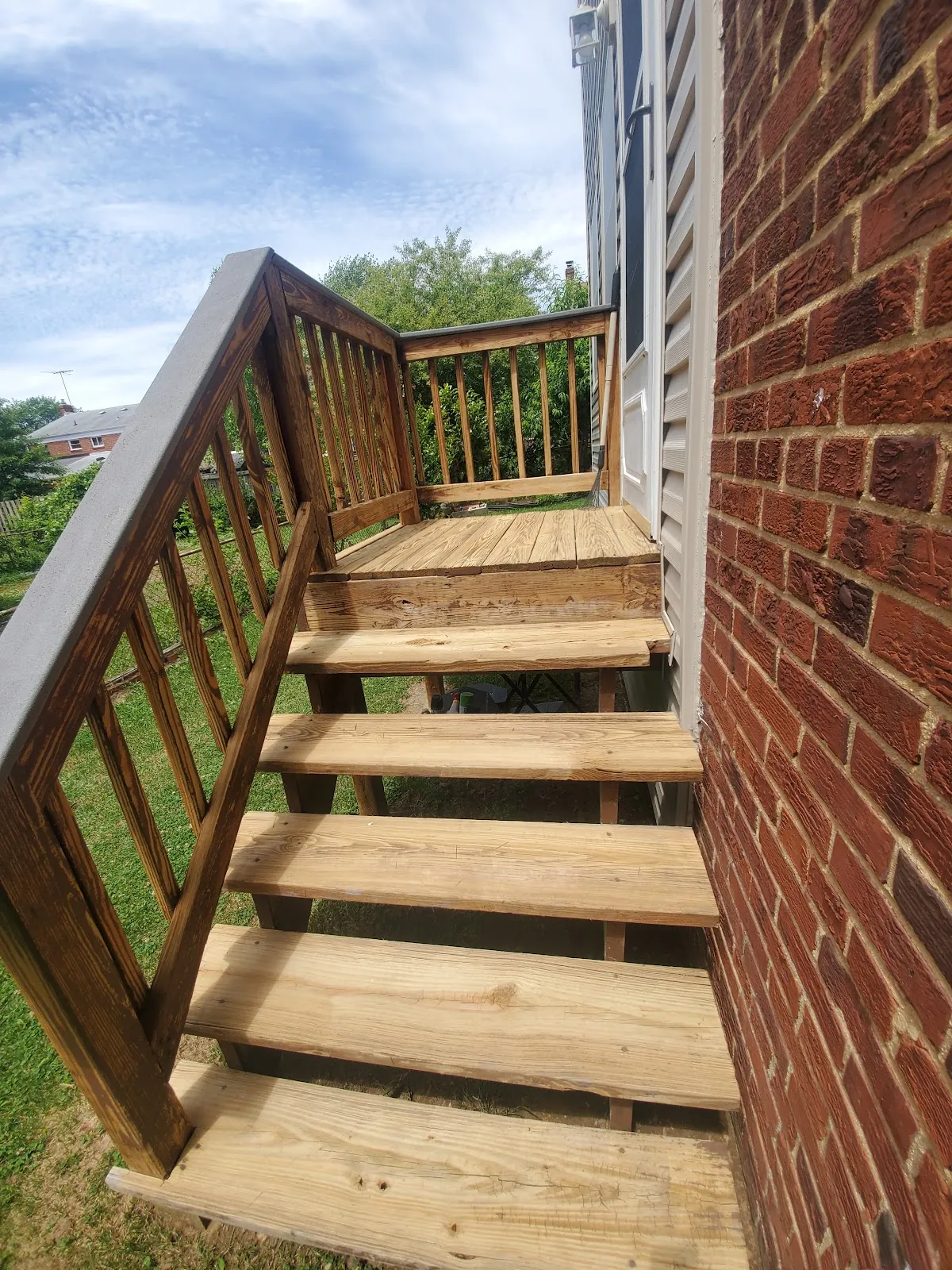 Rebuilt wooden deck stairs and railing against a brick house