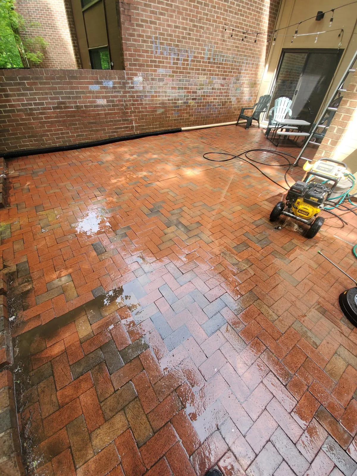 Herringbone brick patio being pressure washed, clean stripe across the pavers